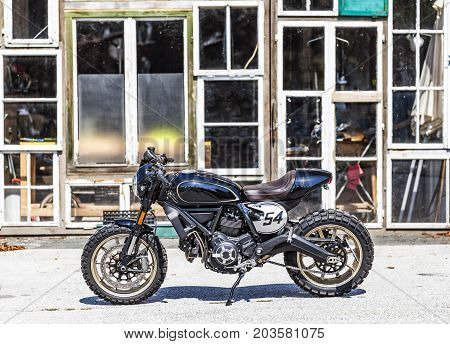 Cool custom made scrambler style cafe racer with standing in front of a glass house