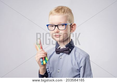 Caucasian boy with blond hair holding pencils in hands and looking up. He is not sure what to fraw