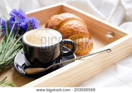 Romantic summer breakfast in bed tray with fresh croissant cup of coffee espresso with milk and bouquet of blue cornflowers. Good morning concept. Enjoy slow life. Traditional continental breakfast.