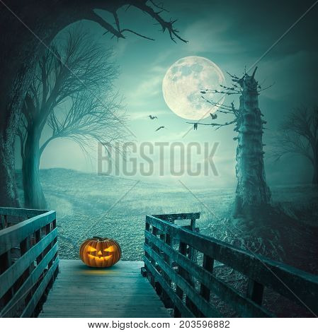 Spooky autumn forest with dead trees old wooden bridge pumpkin bats and roots at full moon night. Halloween concept.