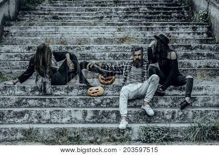 Halloween people or friends on stony stairs. Women with pumpkin heads. Halloween jack o lantern symbols. Bearded man sitting with girls. Holiday celebration concept.