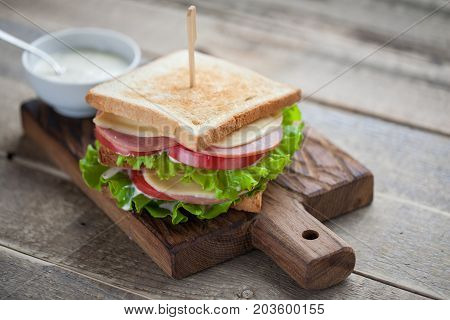Close-up Big Sandwich With Ham, Cheese, Tomatoes, Salad And White Sauce On Toasted Bread On A Rustic