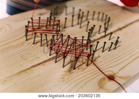 close-up of nails driven into a wooden board, they are impregnated with woolen threads, needlework hobby, selective focus