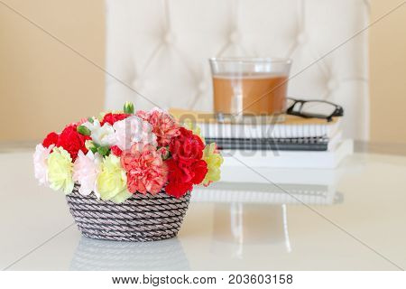 Colorful carnations in brown vase books and candle on marble table.