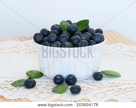 Closeup fresh orgarnic blueberries antioxidant in a white bowl on lace and wooden table.