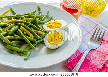 Cooked green beans with boiled eggs in white plate. Healthy vegetarian food concept.