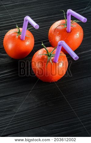Three Ripe Red Tomatoes with Straws on Black Wooden Table Close-up. Fresh Juice Healthy Food Concept. Tomato as a Vessel with Fresh Juice. Background with a Blank Space for Text