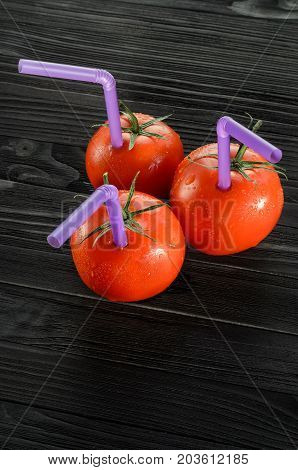 Three Ripe Red Tomatoes with Straws on Black Wooden Table Close-up. Fresh Juice Healthy Food Concept. Tomato as a Vessel with Fresh Juice. Background with a Blank Space for Text