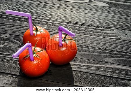 Three Ripe Red Tomatoes with Straws on Black Wooden Table Close-up. Fresh Juice Healthy Food Concept. Tomato as a Vessel with Fresh Juice. Background with a Blank Space for Text