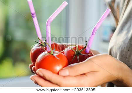 Three Ripe Red Tomatoes with Straws in Woman Hands on Bright Background. Fresh Juice Healthy Food Concept. Tomato as a Vessel with Fresh Juice