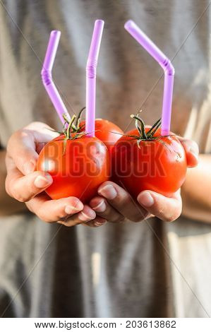 Three Ripe Red Tomatoes with Straws in Woman Hands on Bright Background. Fresh Juice Healthy Food Concept. Tomato as a Vessel with Fresh Juice