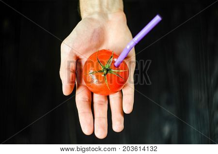 One Red Tomato with Straw on Man Hand on Black Background. Fresh Juice Healthy Food Concept. Tomato as a Vessel With Fresh Juice