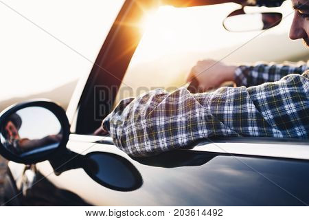 Man Sits Behind Rudder In Cabriolet And Looks In Rear-view Mirror. Hipster Driving Modern Cabriolet