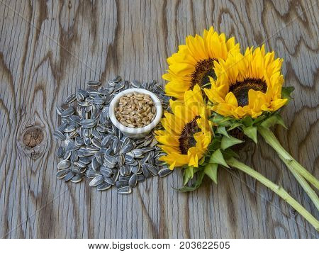Organic sunflower seeds and beautiful flowes on wood tablel close-up