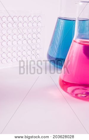 research, science and clinic background. 96 well micro plate and  laboratory beakers with colorful liquids and reagents.