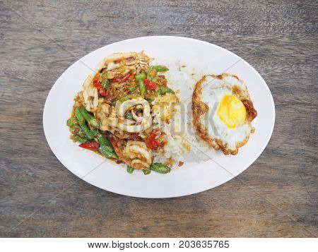 Seafood curry (stir basil) and fried egg over rice on wooden table Thai food.