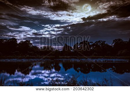 Sky With Many Star And Full Moon Above Silhouettes Of Trees And Lake.