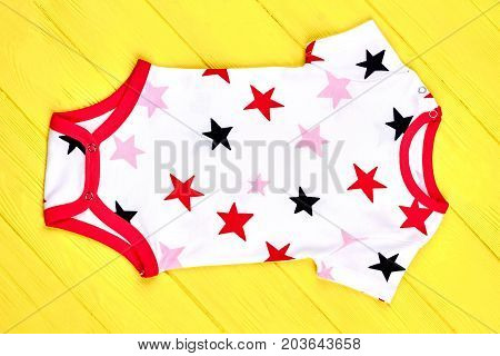 Newborn kids white patterned bodysuit. Baby soft stars print romper on yellow wooden background. Infants high quality outfit.