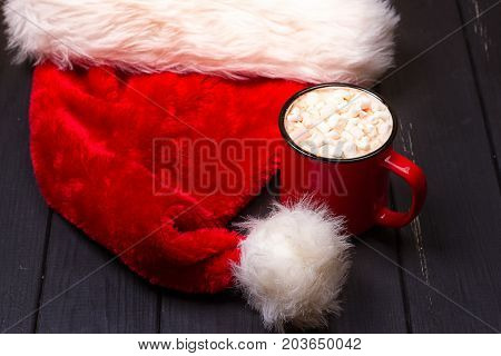 Hot chocolate with marshmallows and cap santa on grunge dark table