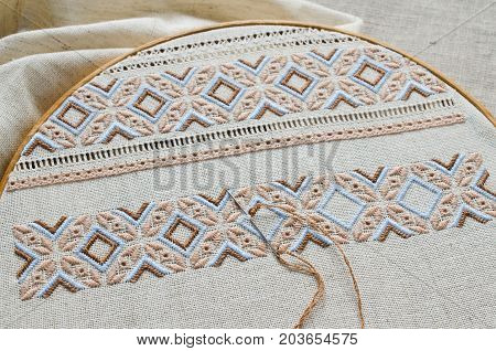 Embroidered fragment on flax by brown and beige cotton threads. Macro embroidery texture flat stitch. Ukrainian ethnic ornament.