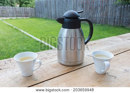 Thermos bottle with two mugs in a garden