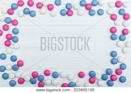 Frame from colorful mint coated candies texture on white wooden background. Top view. Copy space