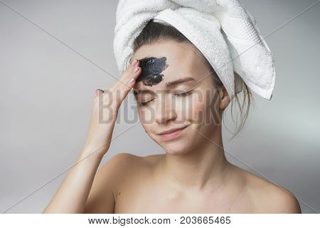 A beautiful girl with a towel on her head smeared a dark ointment on her forehead