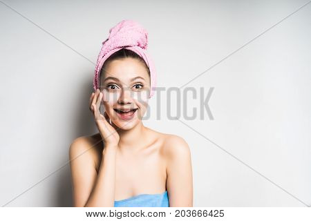 A surprised woman with a towel on her head looks after the skin. Holds a hand near the face