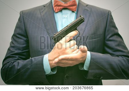Elegant hitman in suit with red bow holds gun in front of himself. Smart Killer reloads the gun.