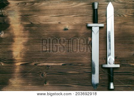 Two swords on burnt wooden surface with copy space background.