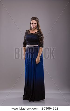 Portrait of a plus size female model posing in black dress over grey background. Beautiful woman with curvy figure.