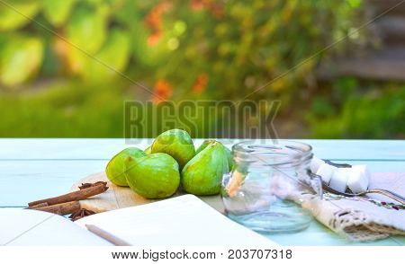 Still life with figs, jam cooking process. Fresh green figs on wooden backround, surrounded by spices, embroidered nupkin, vintage spoon, a glass container for jelly. Notebook with copy space.