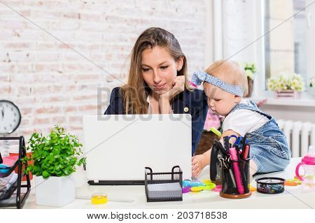 Working together is so fun Cheerful young beautiful businesswoman looking at laptop while sitting at her working place with her little daughter
