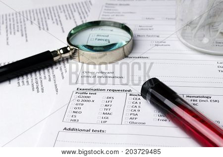 magnifying glass beaker blood sample test tube and patient information form on desk heart healthcare technology medical diagnosis blood test medical report record and history patient concept