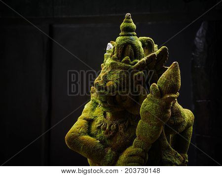Balinese Carved Stone Statue of Rakasa covered with green moss. at Hindu Temple.