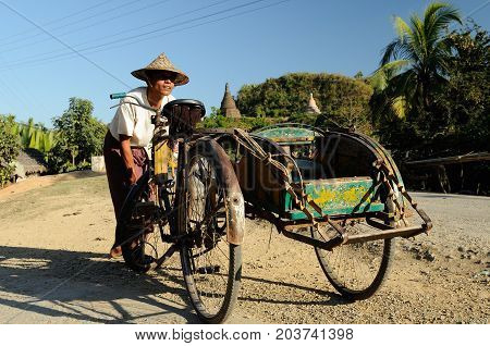 MRAUK-U MYANMAR - 25 JANUARY 2011: The driver of the rickshaw is pumping the wheel up on a dirt road in Burma
