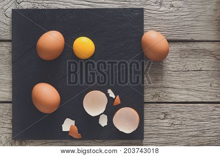 Fresh chicken brown home eggs top view with cracked eggshell and yolk on rustic slate black plate on wood background. Natural healthy food and organic cooking ingredients