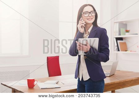 Making business call. Cheerful ceo businesswoman talking on mobile in modern office and holding tablet, copy space
