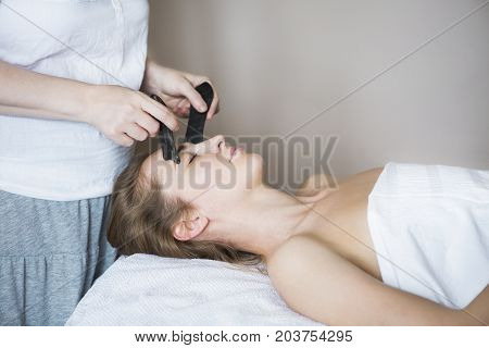 Young woman have face guasha treatment at asian beauty clinic