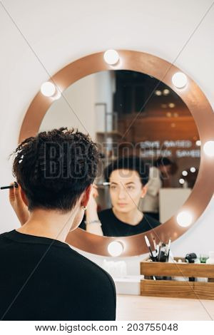 Attractive woman primp at the mirror with lamps in the beauty studio. A happy satisfied customer of make-up and hairstyle service.