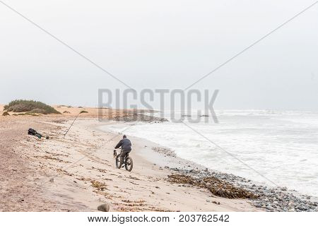 SWAKOPMUND NAMIBIA - JUNE 30 2017: A man on a bicycle a dog and an angler at Swakopmund in the Namib Desert on the Atlantic Coast of Namibia