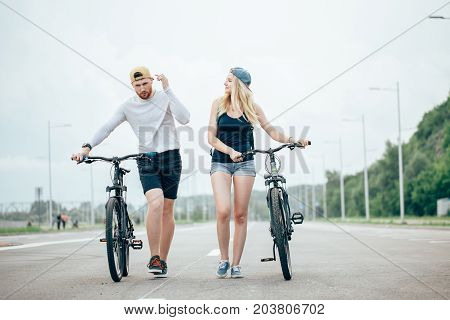 Man And Woman Walk Their Bikes Down The Road
