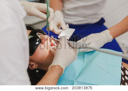 The male dentist with a female assistant helps to treat the teeth of a woman patient in a clinic in the office close-up