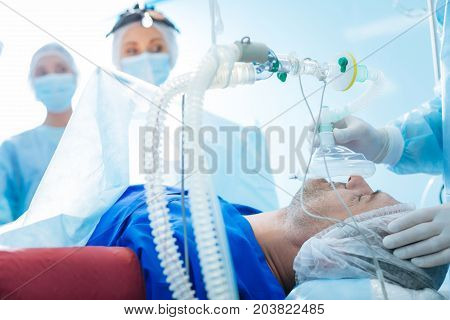 Emergency help. Competent doctor standing near his patient and putting oxygen mask on his face while going to treat him