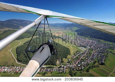 Hangglider pilot flies over small alpine town in mountain valley onboard shot with action camera.