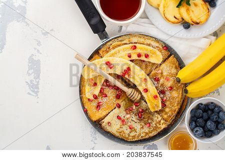 Sweet crepes with banana, honey and pomegranate seeds in a frying pan. Delicious family breakfast concept. Space for text