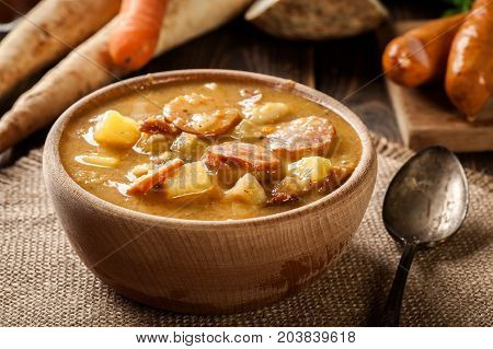 Wooden Bowl Of Split Pea Soup With Sausage And Potatoes