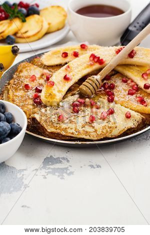 Sweet crepes with banana, honey and pomegranate seeds in a frying pan. Delicious family breakfast concept. Space for text