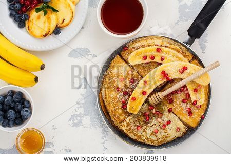 Sweet crepes with banana, honey and pomegranate seeds in a frying pan. Delicious family breakfast concept. Space for text