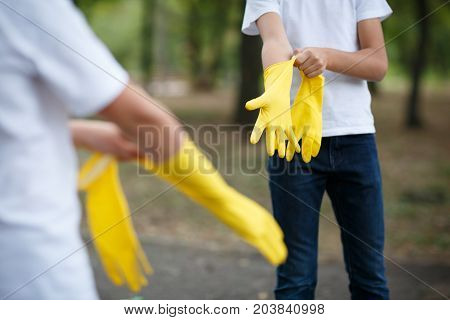 Team work of outdoors cleaning. Environmental protection. Closeup cropped portrait. Getting started cleaning. Yellow rubber cleaning gloves closeup. Workhouse concept. Helping team.